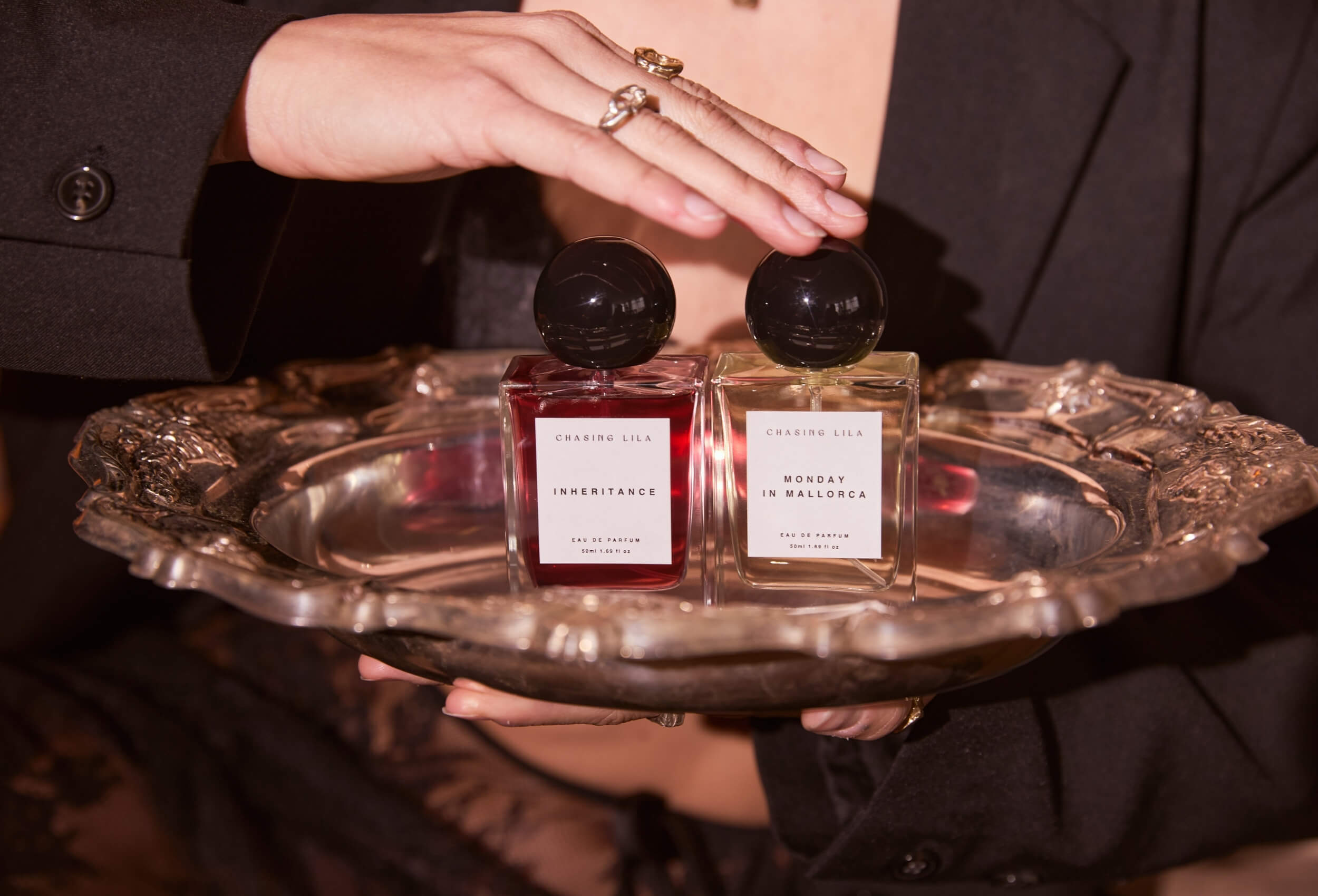 Clean citrus and floral luxury perfume by Chasing Lila - on a silver tray held by a person wearing a black coat.