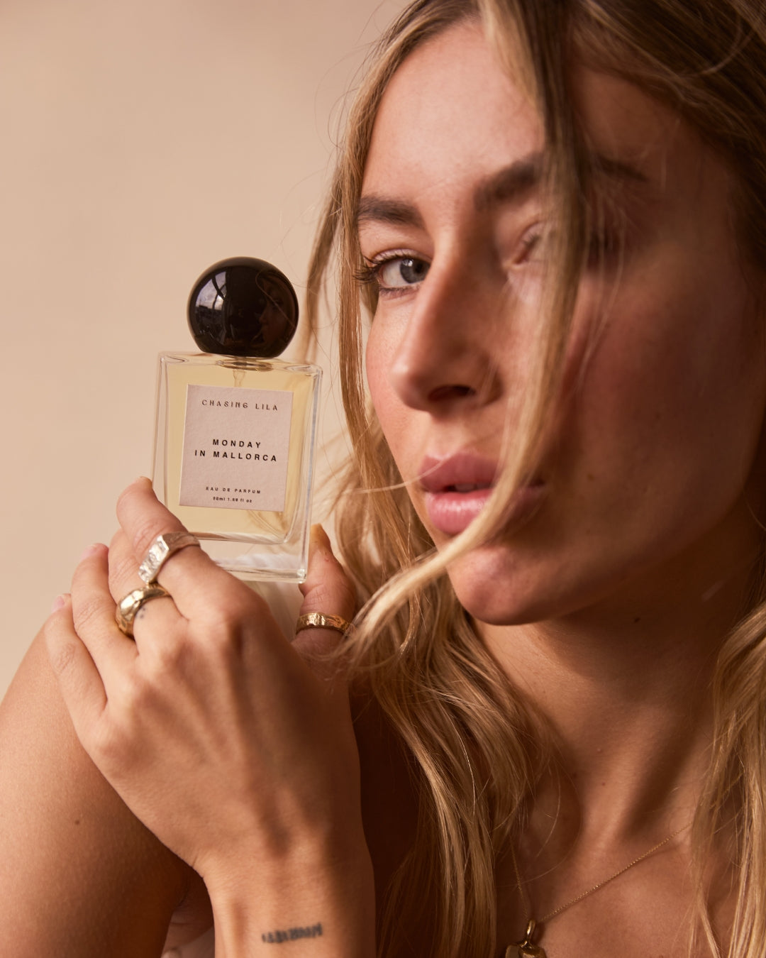 Woman holding a perfume bottle Monday in Mallorca with a neutral background